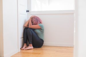 picture of a woman sitting on the floor, covering her face from grief due to recurrent miscarriage or recurrent pregnancy loss